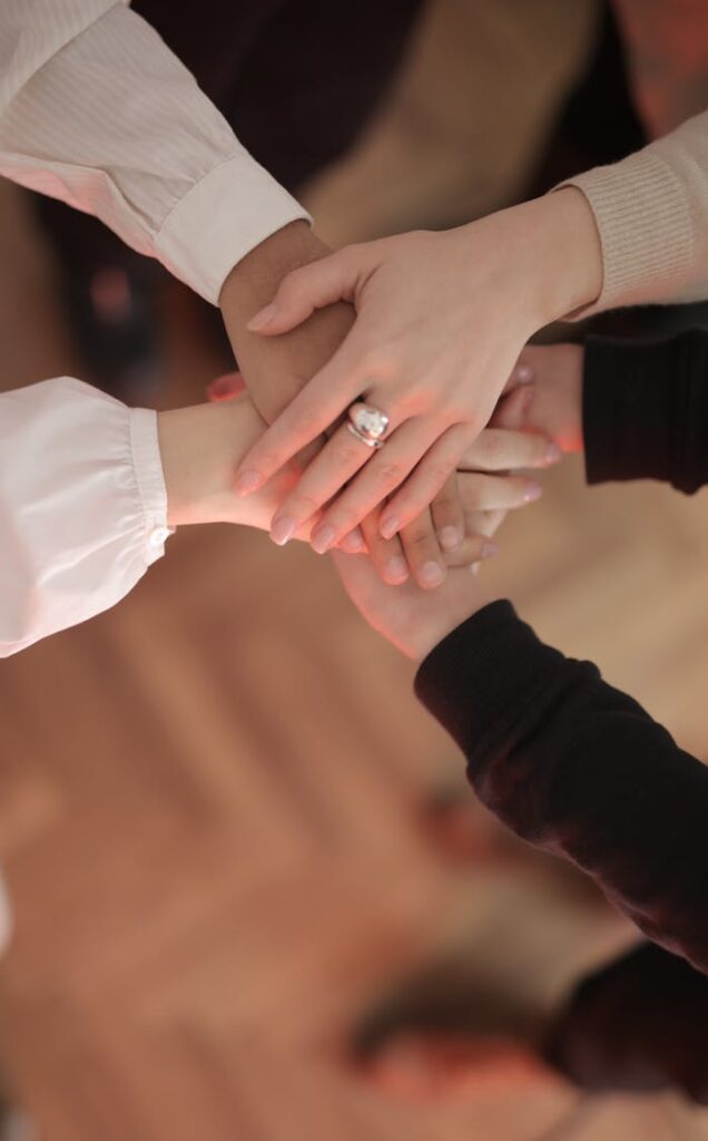 pexels photo 3830752 Top view of faceless friends in different clothes stacking hands together while standing on wooden floor indoor on sunny day