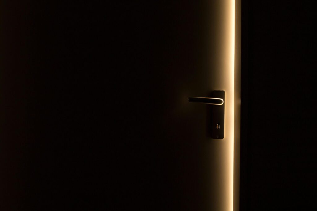 A dark room with a door slightly ajar, revealing a glowing light through the opening.