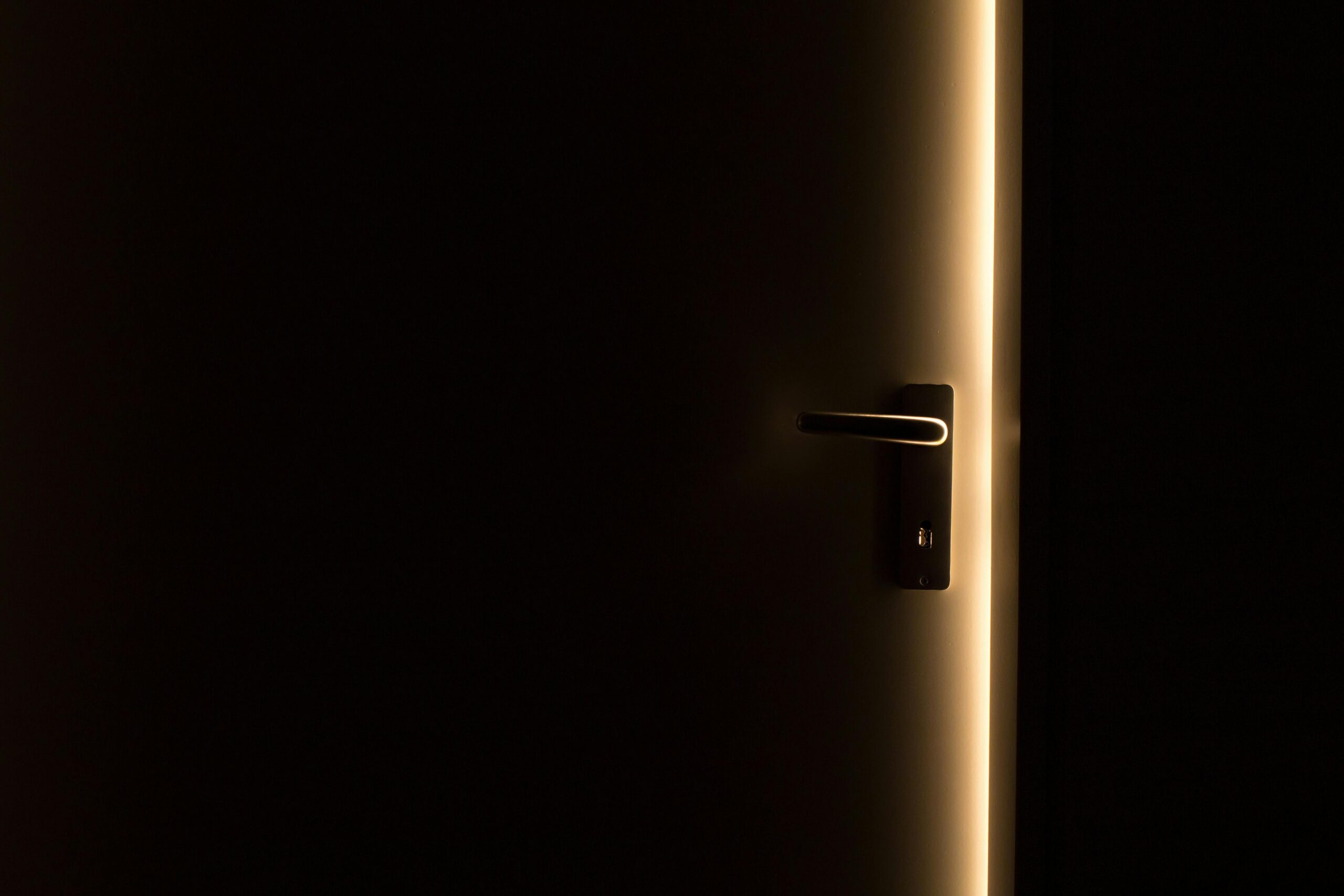 Why Leaving Is Not the End of Abuse: Understanding Post-Exit Trauma A dark room with a door slightly ajar, revealing a glowing light through the opening.